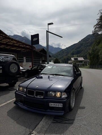 Schwarzer BMW E36 vor der COB Garage, Berge im Hintergrund