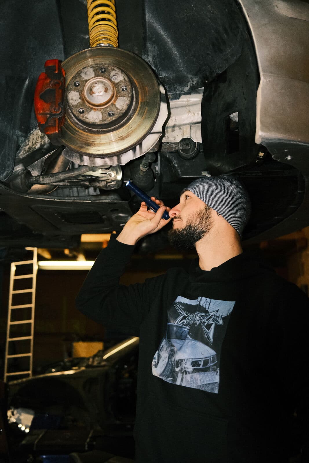 Mechaniker der COB Garage leuchtet mit der Taschenlampe unter ein aufgebocktes Auto