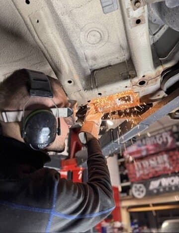 Mechaniker mit Gehörschutz schleift am Unterboden, Funken fliegen