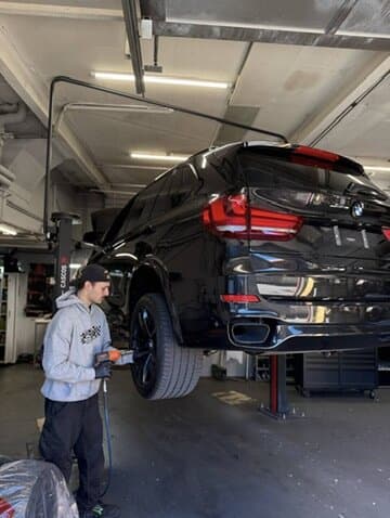 Schwarzer BMW X5 auf der Hebebühne, ein Mechaniker am Rad