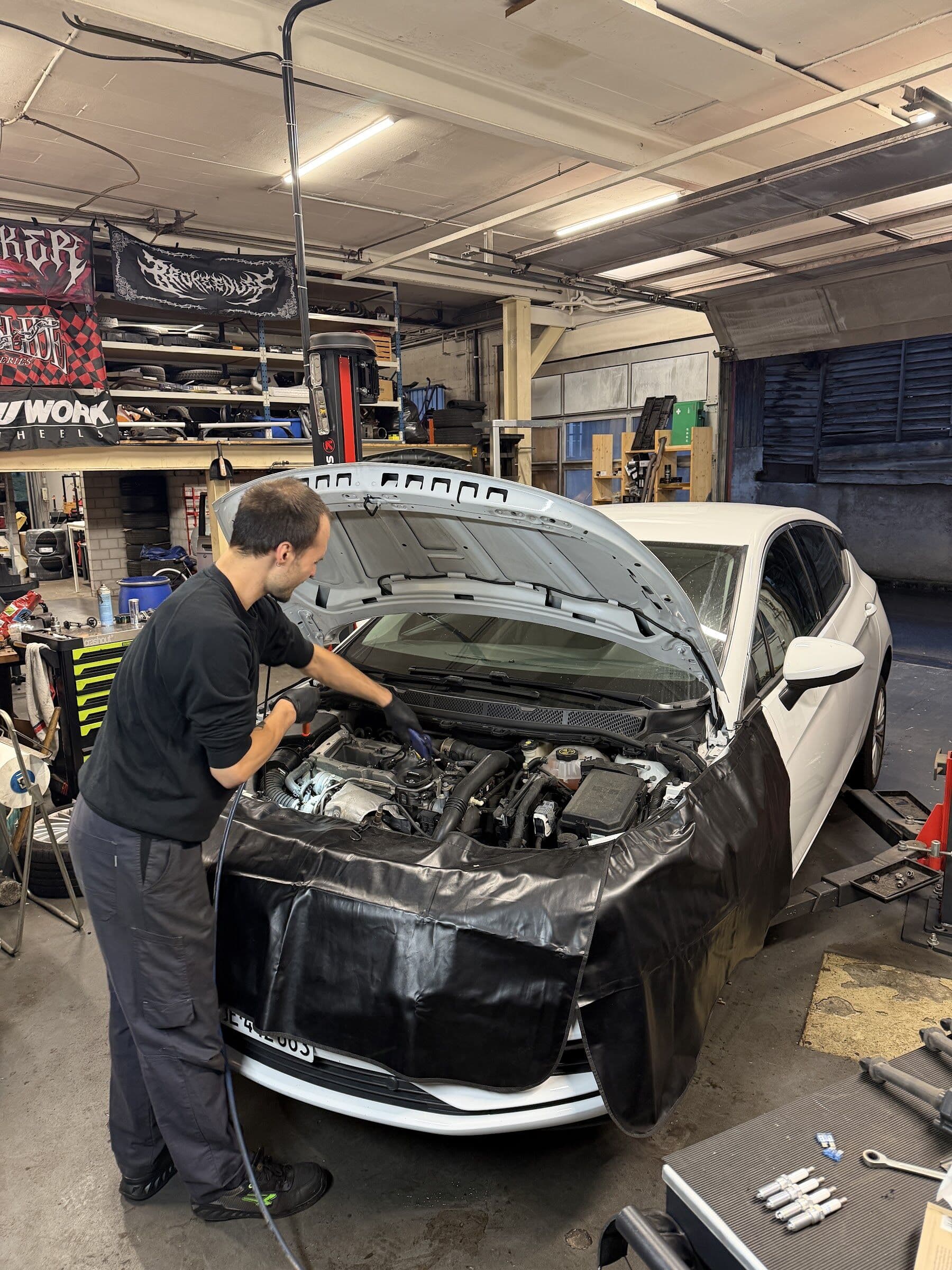 Mechaniker der COB Garage arbeitet im Motorraum eines weissen Autos in der Werkstatt